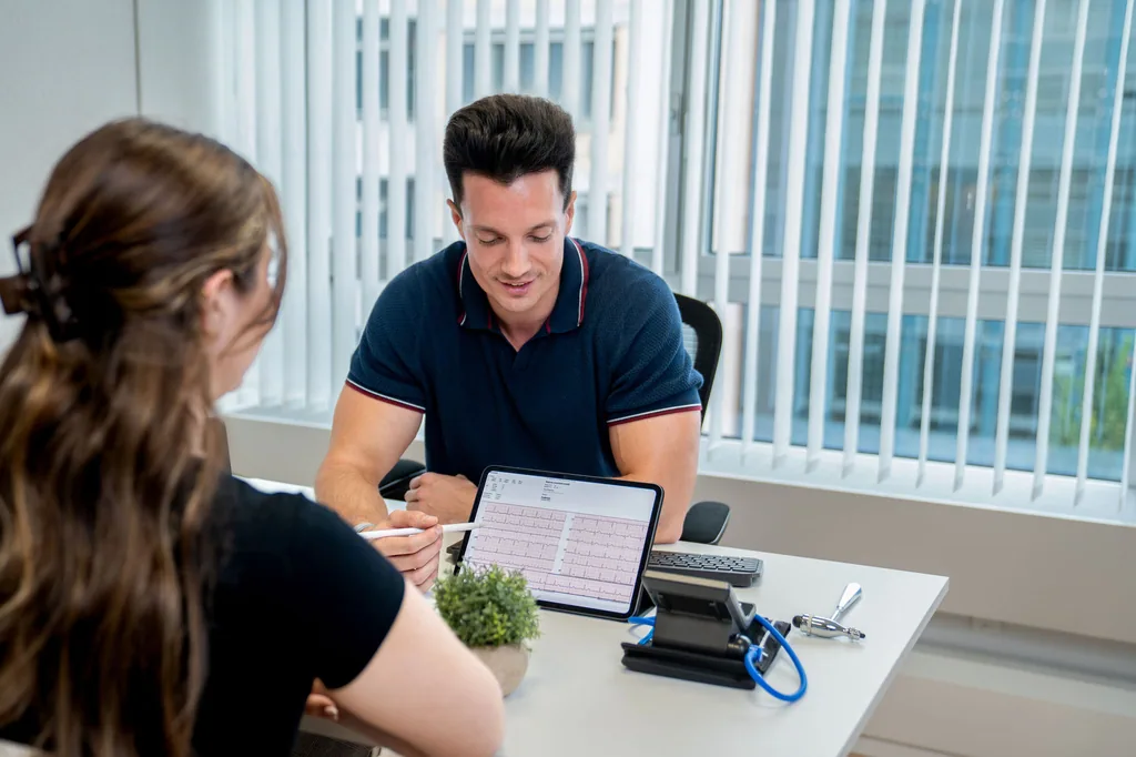 Arzt bespricht ein EKG auf dem Tablet mit einer Patientin